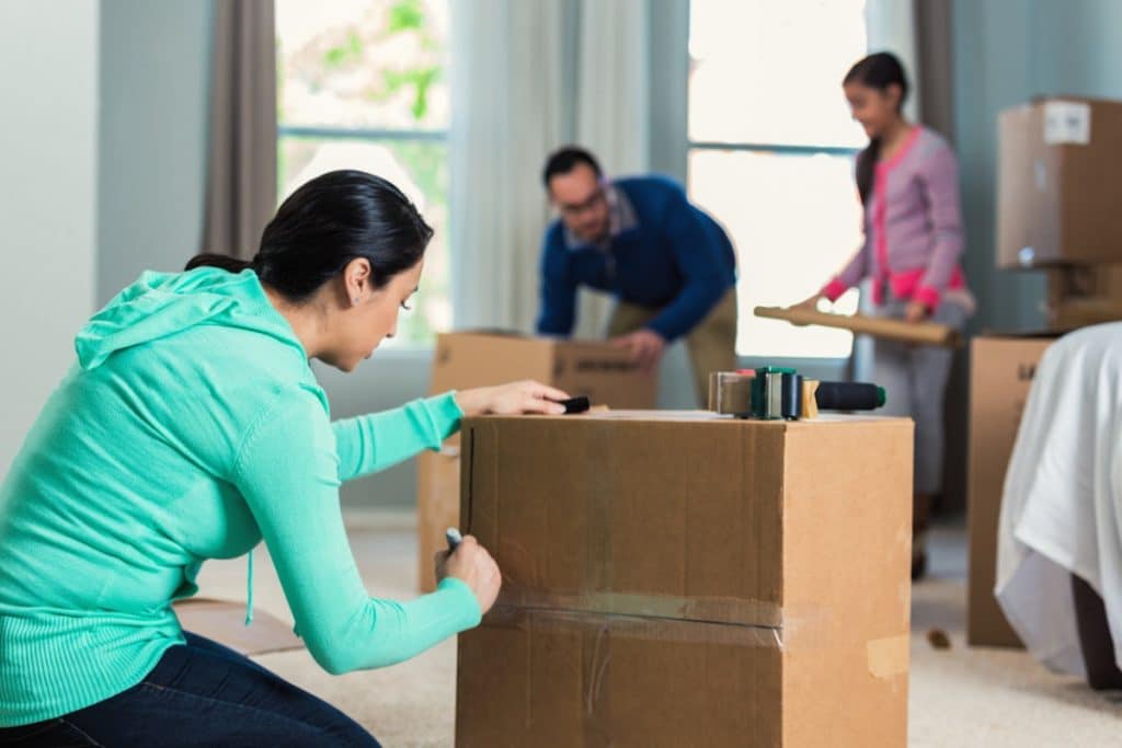 Une femme étiquetant une boîte de déménagement pendant que sa famille emballe.